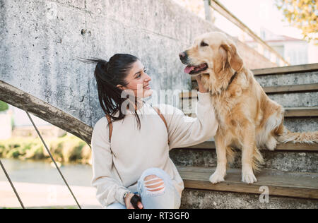 Souriante jeune femme caressant son chien golden retriever dans les escaliers à l'extérieur Banque D'Images