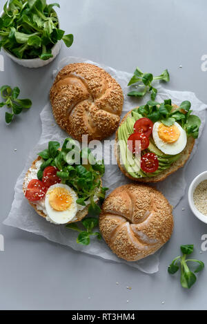 Sandwiches bagel au fromage à la crème, Avocat, tomates, œuf et verts sur fond de bois gris. Focus sélectif. La saine alimentation ou la nourriture végétarienne co Banque D'Images