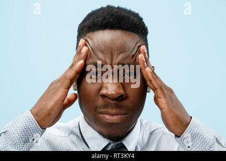 L'homme ayant des maux de tête. Isolé sur fond bleu. L'african businessman standing avec douleur isolé sur fond bleu à la mode studio. La moitié des hommes portrait en pied. Les émotions humaines, l'expression faciale concept. Banque D'Images