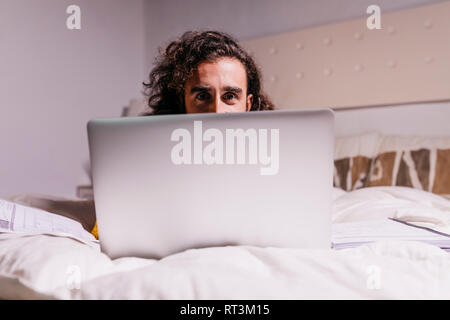 Portrait de jeune homme au lit à la maison à l'aide d'ordinateur portable Banque D'Images