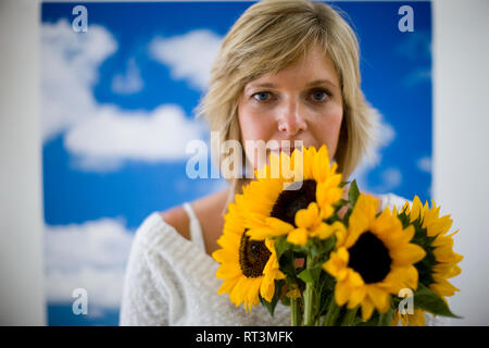 Portrait of a young woman holding a bouquet de tournesols en face d'un ciel nuageux en toile de fond. Banque D'Images