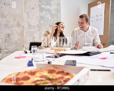 Rire des collègues ayant pause déjeuner avec la pizza dans la salle de conférence Banque D'Images