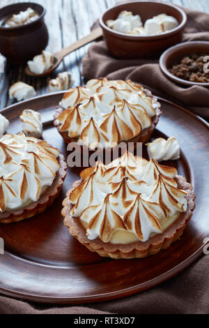 Close-up de tartes au citron meringuée mini chocolat doré avec des pics de meringue servi avec café, mini guimauves et brown sucre biologique sur l'onglet en bois Banque D'Images