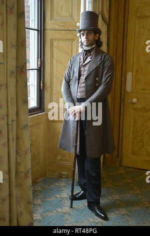 Un beau jeune homme de l'époque victorienne dans un costume historique se dresse contre une toile de fond d'un portrait- il a un haut de forme et canne à sucre Banque D'Images