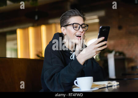 Femelle jeune hipster raccourci lecture blogger choqué news dans message sur téléphone mobile Banque D'Images