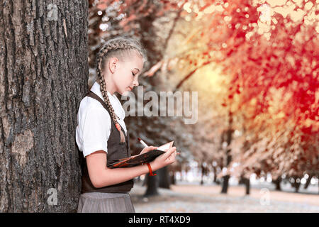 Lycéenne adolescent lisant un livre dans un parc près d'un arbre. devoirs enseigne aux couleurs. Banque D'Images