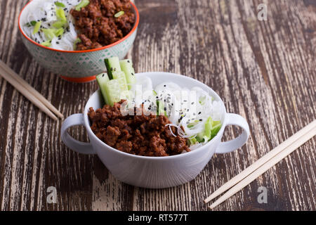 Bol de style asiatique avec du boeuf haché, pâtes de riz, le concombre, les oignons verts et les graines de sésame, brunch sain plat avec viande et légumes Banque D'Images