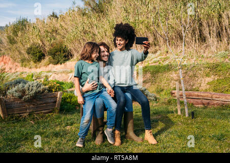 Famille heureuse assis sur un banc dans un jardin, la mère en tenant vos autoportraits Banque D'Images