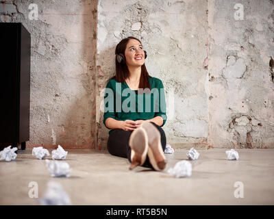 Smiling woman sitting on floor office d'écouter de la musique Banque D'Images