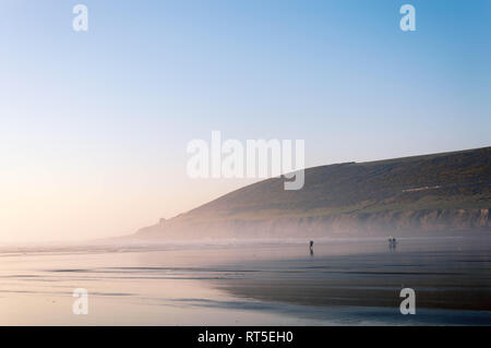 Surfers silhouetted marche sur la plage au coucher du soleil sur une chaude journée de février 2019. Saunton Sands, Devon, UK. 27 févr. 2019. Banque D'Images