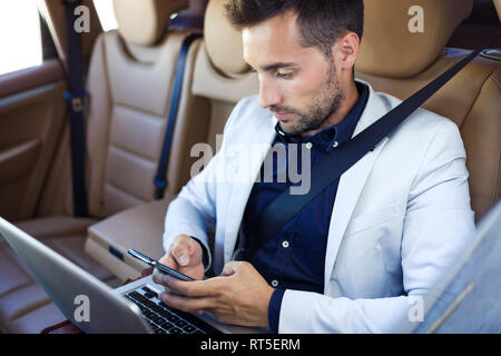 Jeune homme d'affaires travaillant à partir de la banquette arrière d'une voiture Banque D'Images