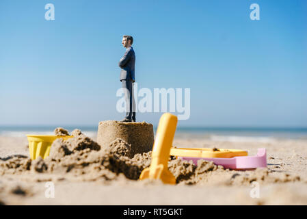 Figurine homme debout sur le sable avec des jouets autour de Banque D'Images