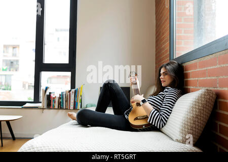 Jeune femme assise sur la table à la maison à jouer de la guitare Banque D'Images