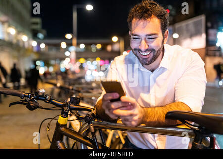 UK, Londres, homme heureux en regardant son téléphone par nuit Banque D'Images