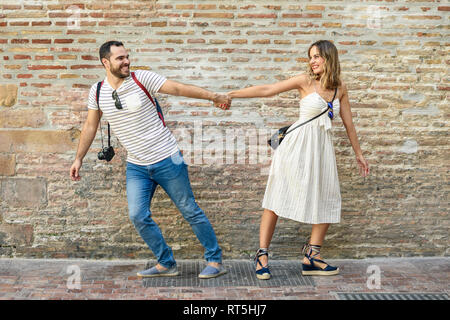 Heureux couple holding hands walking en sens opposé à brick wall Banque D'Images