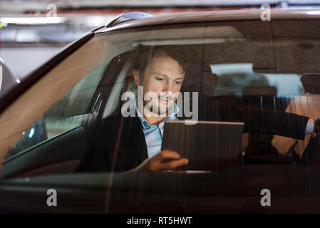 Businessman sitting in car la nuit, using digital tablet Banque D'Images