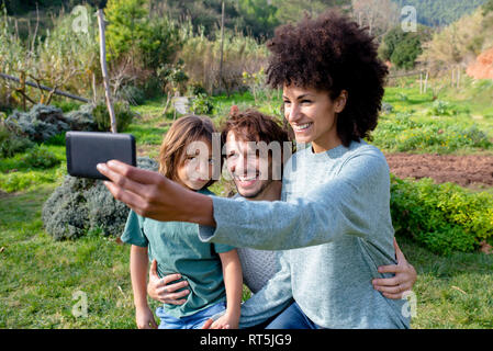 Famille heureuse assis sur un banc dans un jardin, la mère en tenant vos autoportraits Banque D'Images