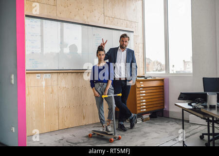 Homme mature et son assistant jouant avec scooter, standing in office in front of white board Banque D'Images