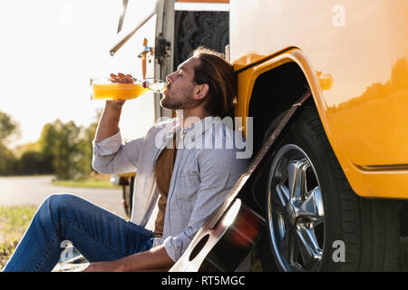 Jeune homme d'un voyage avec son camping-car, le fait de prendre une pause, de boire du jus Banque D'Images