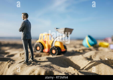 Figurine homme debout sur le sable avec toy digger, l'investissement dans l'accession à la propriété Banque D'Images