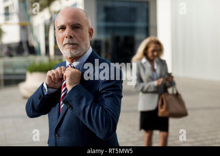 Senior businessman ajustant sa cravate avec man in background Banque D'Images