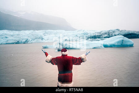 L'Islande, vue arrière d'un homme déguisé en Père Noël debout à un glacier soulevant ses bras Banque D'Images