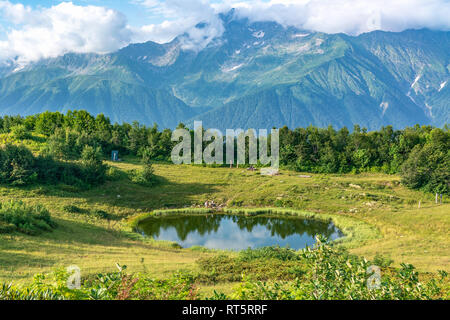 Vue d'une clairière de montagne avec un lac miroir transparent, et les touristes, entouré de pelouses et d'arbres et de hautes montagnes avec des sommets enneigés dans le Banque D'Images