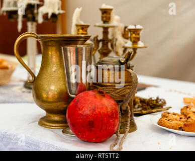 Une grenade, fruit rouge vintage metal beer mug, un verre de vin et une cruche. Certains des tartes sur la table, des chandeliers en arrière-plan Banque D'Images