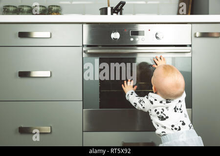 Petit enfant jouant avec cuisinière électrique dans la cuisine. La sécurité de bébé dans la cuisine Banque D'Images