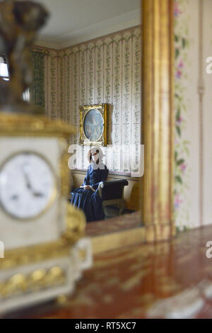 Une vieille femme se distingue par un style Victorien très cheminée décorée et regarde dans un miroir- il y a une horloge bronze doré d'or disant que c'est 4h00 à côté d'elle. Banque D'Images