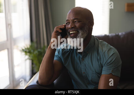 Senior man talking on mobile phone in living room Banque D'Images