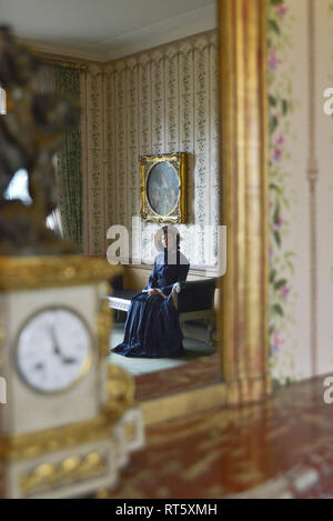 Une vieille femme se distingue par un style Victorien très cheminée décorée et regarde dans un miroir- il y a une horloge bronze doré d'or disant que c'est 4h00 à côté d'elle. Banque D'Images