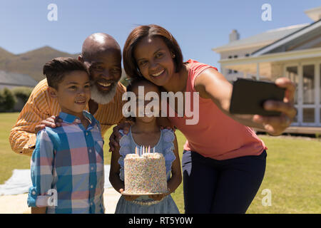 Multi-generation family en tenant avec selfies téléphone mobile tout en célébrant l'anniversaire de la petite-fille Banque D'Images