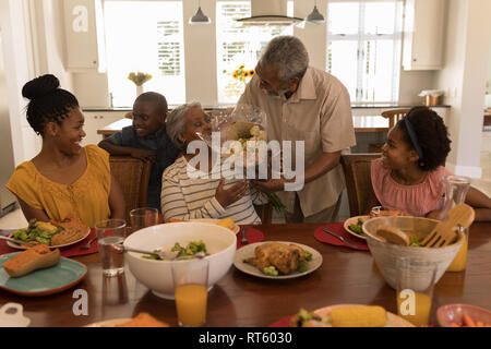 Hauts man giving bouquet de fleurs senior woman on dining table Banque D'Images