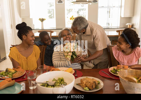 Hauts man giving woman bouquet de fleurs tout en ayant des repas sur table à manger Banque D'Images