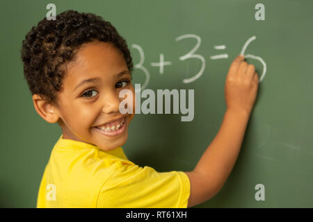 Happy schoolboy looking at camera alors que faire des mathématiques dans une classe panneau greenboard sur Banque D'Images