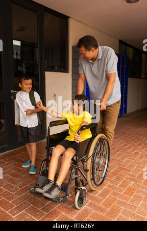 En d'écolier avec fauteuil roulant sont mâles et de camarade dans le couloir Banque D'Images