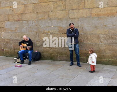 Funny little girl et l'homme qui joue de la guitare dans une rue proche de la cathédrale. Santiago de Compostela, Espagne, 22 février 2019. Banque D'Images