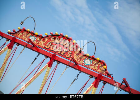 Haut de la balançoire bateau fun fair ride en rouge lumineux contre un ciel bleu à une fête foraine en Angleterre Banque D'Images