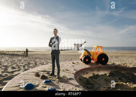 Figurine homme debout sur le sable avec toy digger, l'investissement dans l'accession à la propriété Banque D'Images