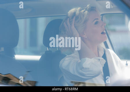 Businesswoman driving car avec la main dans les cheveux Banque D'Images