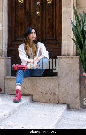 Portrait de jeune femme portant des bottes rouges assis sur l'étape devant la porte d'entrée de Banque D'Images