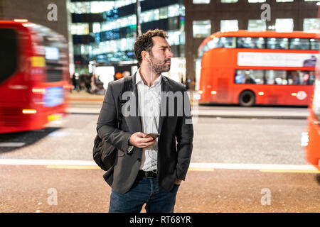 UK, Londres, homme debout à côté d'une rue animée le soir Banque D'Images