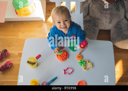 Portrait of smiling baby girl Playing with modelling clay dans la chambre des enfants Banque D'Images