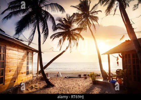 Chalet en bois avec vue sur la mer en complexe hôtelier tropical avec des cocotiers et des transats sur la plage au coucher du soleil Banque D'Images