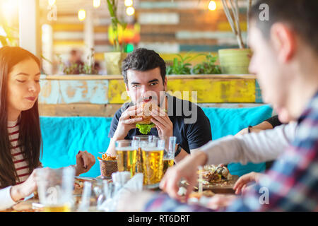 Groupe d'amis, manger et boire de la bière à burger restaurant - jeune homme jouissant burger et compagnie d'amis au restaurant fast food Banque D'Images