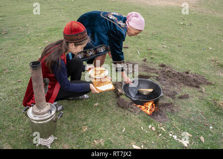 Les femmes en tenue traditionnelle kazakh baursaki friture dans un champ sur un feu de bois, retournerais sans hésiter, Kazakhstan Banque D'Images