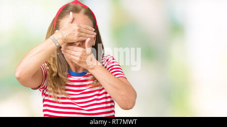 Belle femme d'âge moyen portant des rayures occasionnels t-shirt sur fond isolé couvrant les yeux et la bouche avec les mains, surpris et choqué. E Cacher Banque D'Images