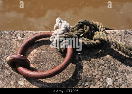 Corde épaisse liée à grande épaisseur d'acier rouillé anneau attaché à la jetée en béton. Banque D'Images