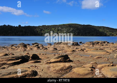 Une île volcanique des roches très côtières exposées à marée basse avec partie plus profonde de port en arrière-plan. Banque D'Images